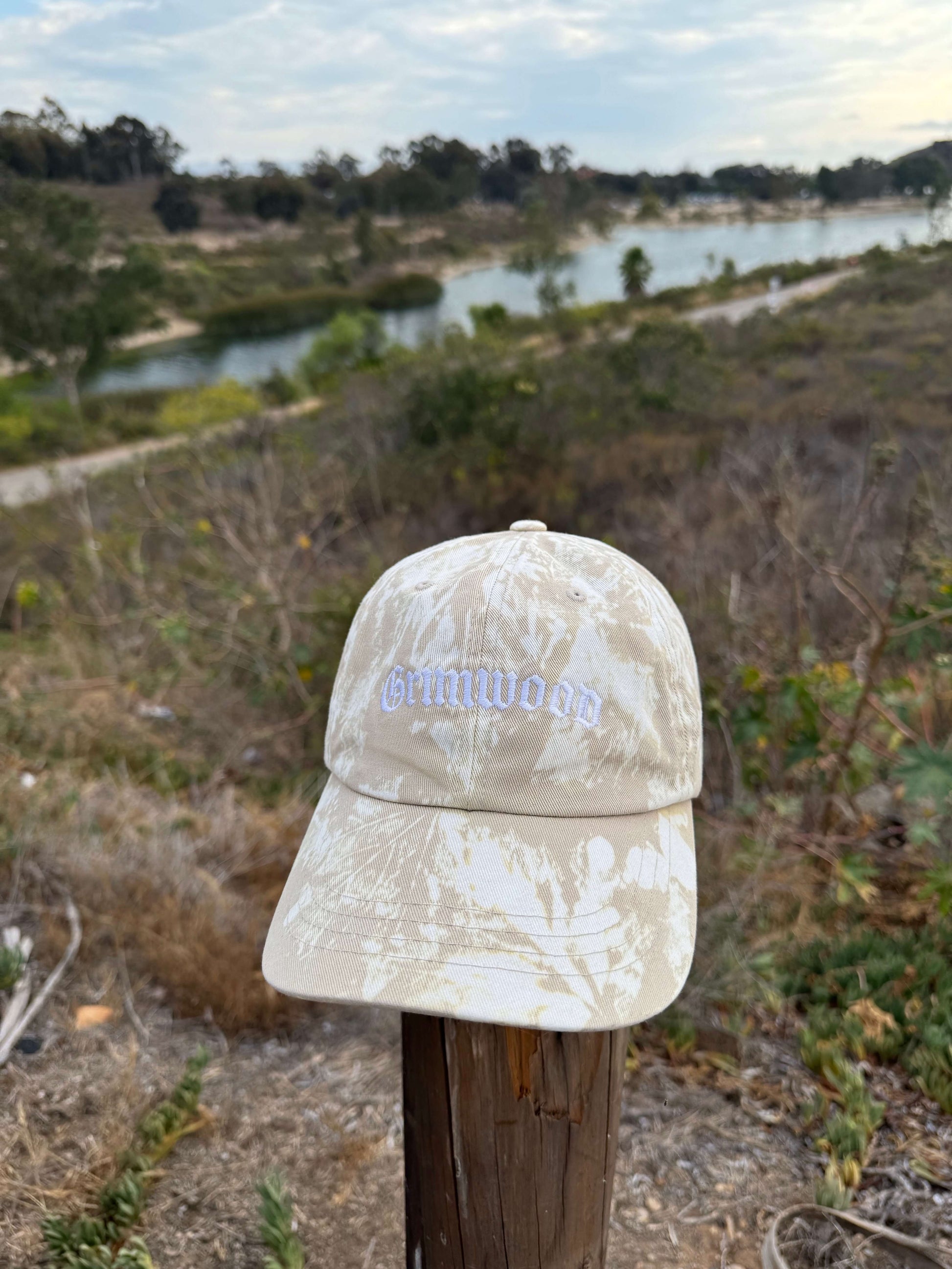 Beige cap with 'Grindworx' logo on a wooden post with a natural landscape in the background